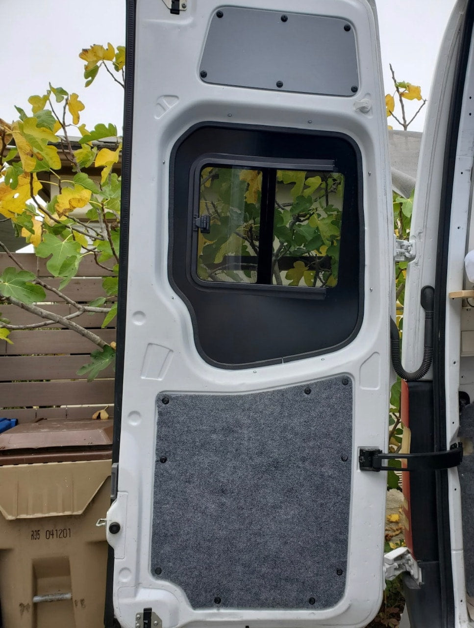 RV rental van's rear door interior, featuring a black-framed window and sound-dampening grey panel. — photo 13