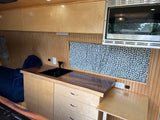 Compact RV rental interior featuring a practical kitchen with sink, microwave, wood cabinetry, and comfortable bed area.