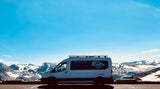 This white RV rental camper van, branded for Van Life KC, rests before grand snow-capped mountains under a clear blue sky.