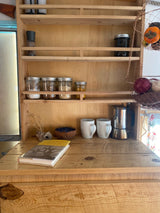 RV rental kitchen setup with wooden shelves, spices, coffee gear, and a hanging produce basket.