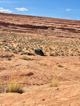 Explore the red rock desert in a black RV rental, parked amidst sparse brush under a bright blue sky.