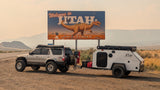 Adventure-ready SUV towing an RV rental camper at Utah's dinosaur welcome sign.
