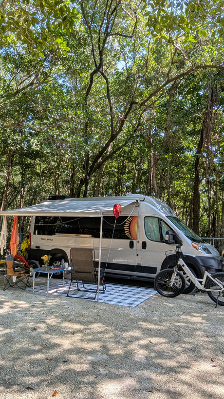 Shaded RV rental campsite setup with an extended awning, outdoor seating, and bicycles for comfortable outdoor living.