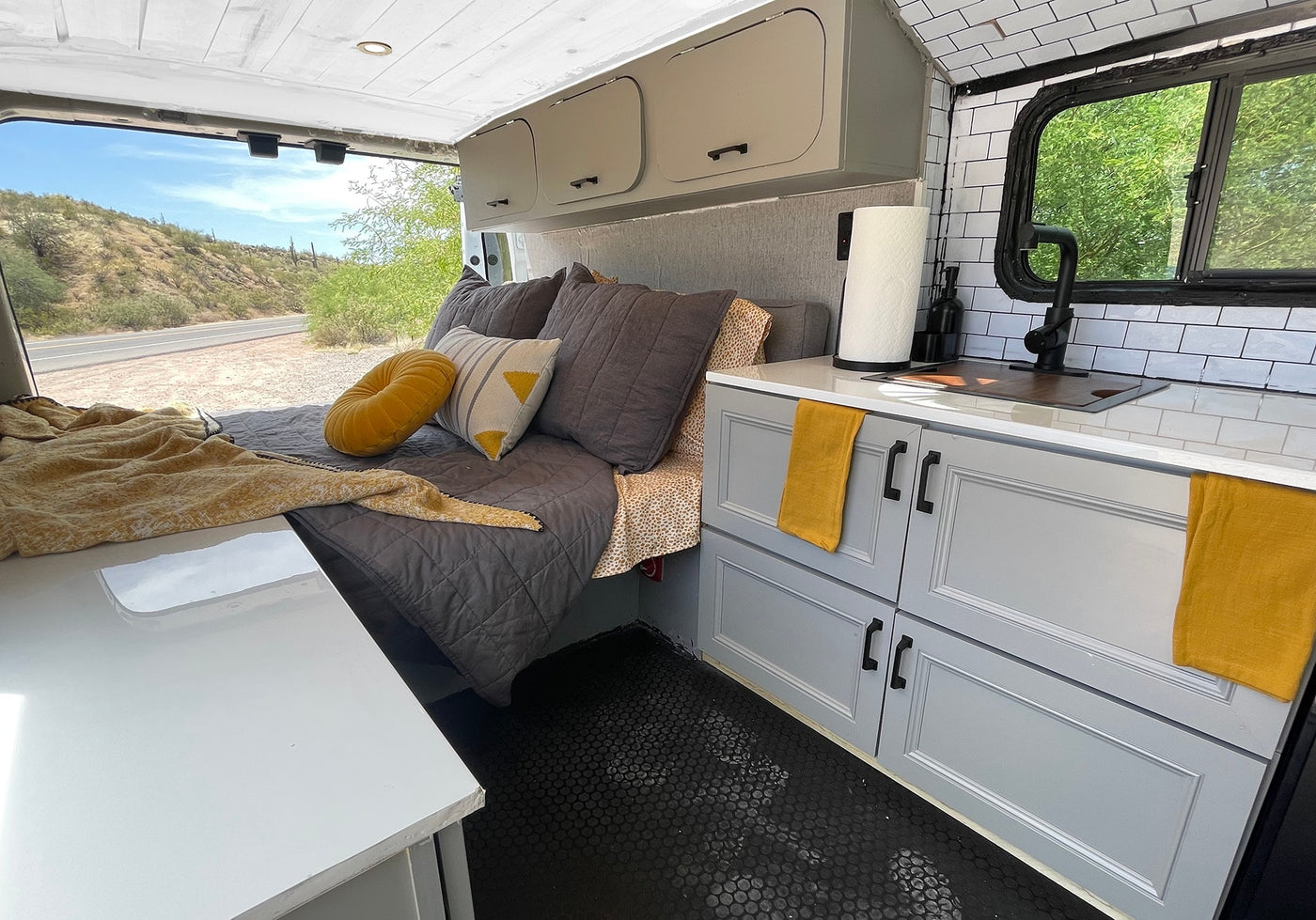 Modern rv rental interior with a cozy bed, fully equipped kitchenette, and desert views. Black hexagonal floor & stylish storage. — photo 10
