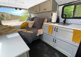 Modern rv rental interior with a cozy bed, fully equipped kitchenette, and desert views. Black hexagonal floor & stylish storage.