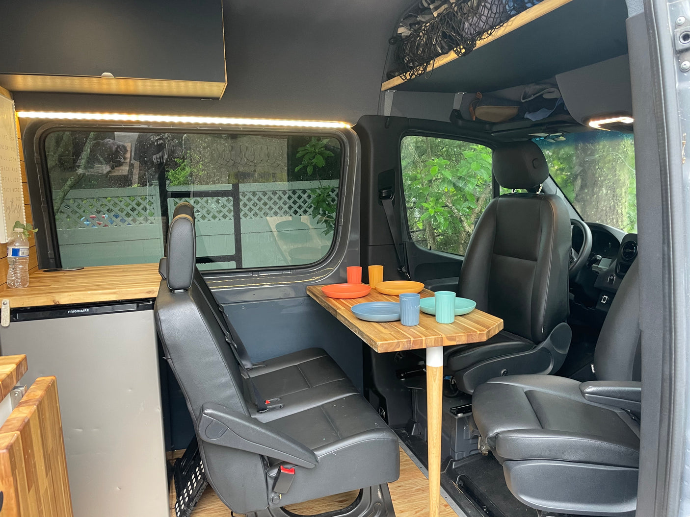 RV rental: inviting camper van interior featuring a dining table with colorful dishes, kitchenette with fridge, and seating.