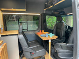 RV rental: inviting camper van interior featuring a dining table with colorful dishes, kitchenette with fridge, and seating.