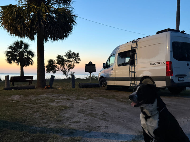 Enjoy an RV rental adventure! A white Geotrek camper van is parked at a scenic waterfront park with a dog at sunset. — photo 9