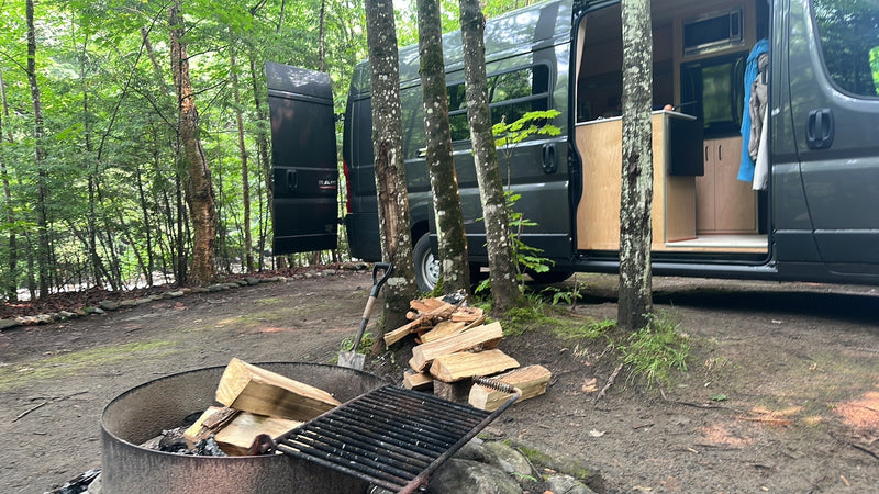 RV rental adventure: Camper van parked at a wooded campsite with a fire pit and stacked firewood, ready for use. — photo 15