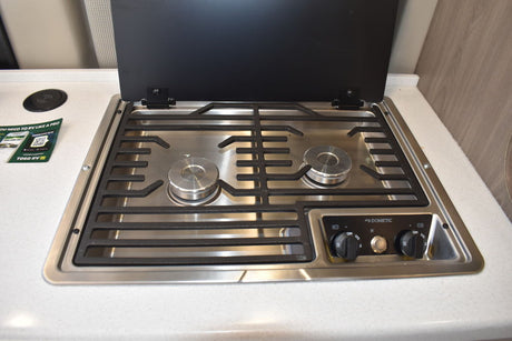 RV rental kitchen features a Dometic two-burner stovetop with grates and control knobs, lid open.