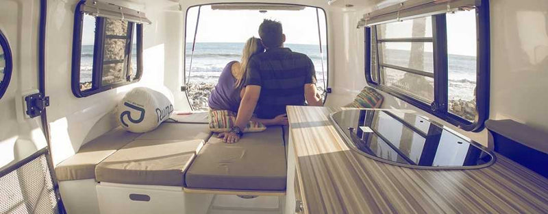  towed by an SUV in a sunny vineyard. Great for outdoor adventures!|Small white RV rental (travel trailer) set up on a sandy site. Features a colorful boogie board & outdoor rug.|Cozy rv rental interior with pink bed — photo 2