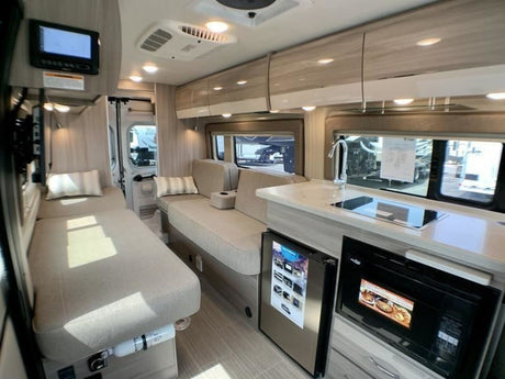 Modern RV rental interior with light wood tones. Features kitchen (sink, cooktop, fridge, microwave) & comfortable bench beds.