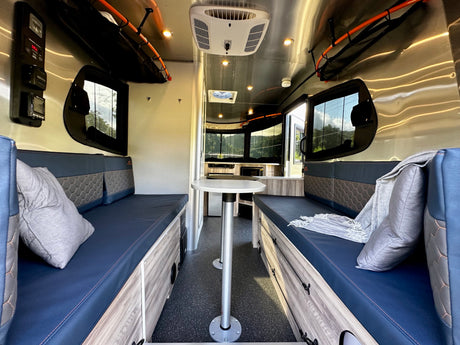 Bright rv rental interior with blue cushioned seating, dining table, and shiny ceiling. A comfy, modern living space.