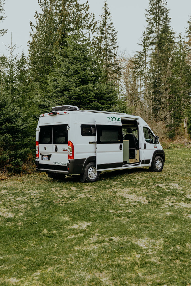 Noma campervan RV rental, a white Ram ProMaster van, parked on grass with its side door open, surrounded by trees. — photo 18