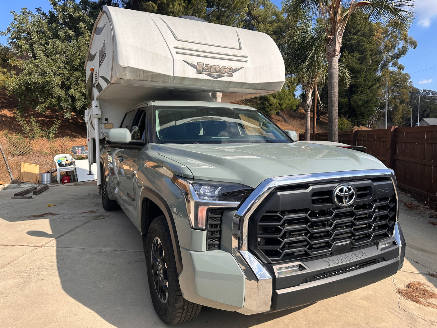 A light-green Toyota Tundra pickup truck with a white Lance truck camper attached, parked on a driveway. Ideal for an RV rental adventure.