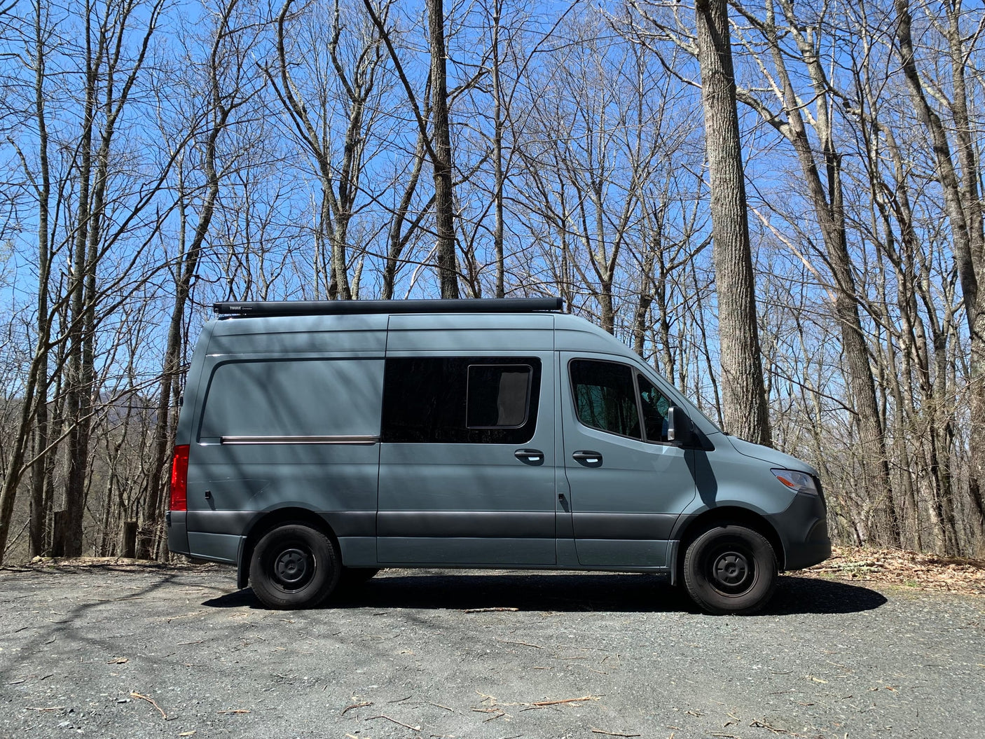 This gray Mercedes-Benz Sprinter rv rental van is parked on a gravel path