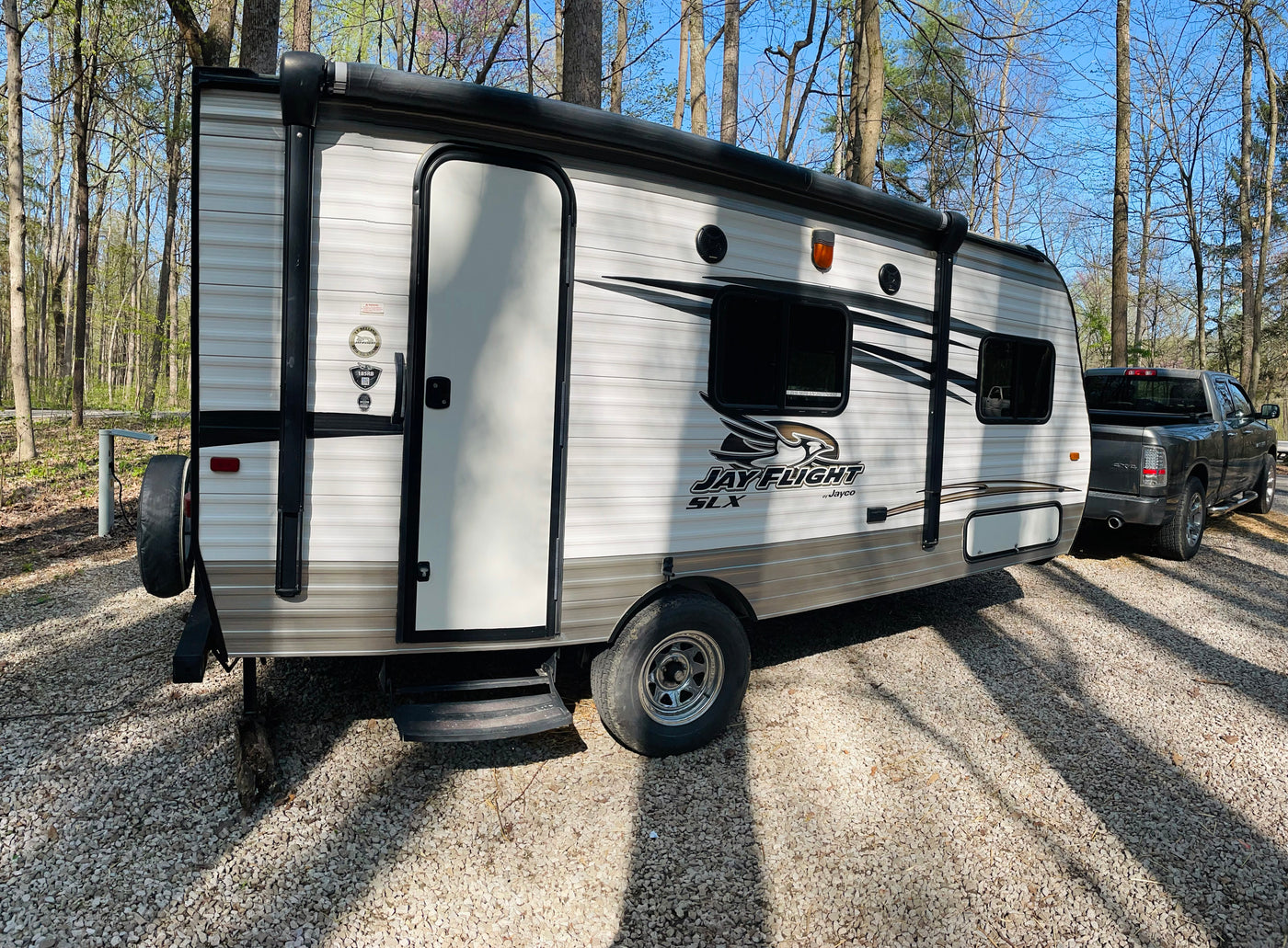 This Jayco travel trailer RV rental, with a pickup truck, is parked on gravel among trees under a clear sky. — photo 13