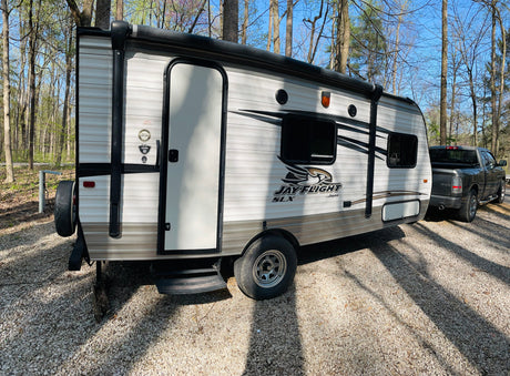 This Jayco travel trailer RV rental, with a pickup truck, is parked on gravel among trees under a clear sky.