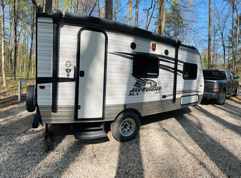 This Jayco travel trailer RV rental, with a pickup truck, is parked on gravel among trees under a clear sky. — photo 13