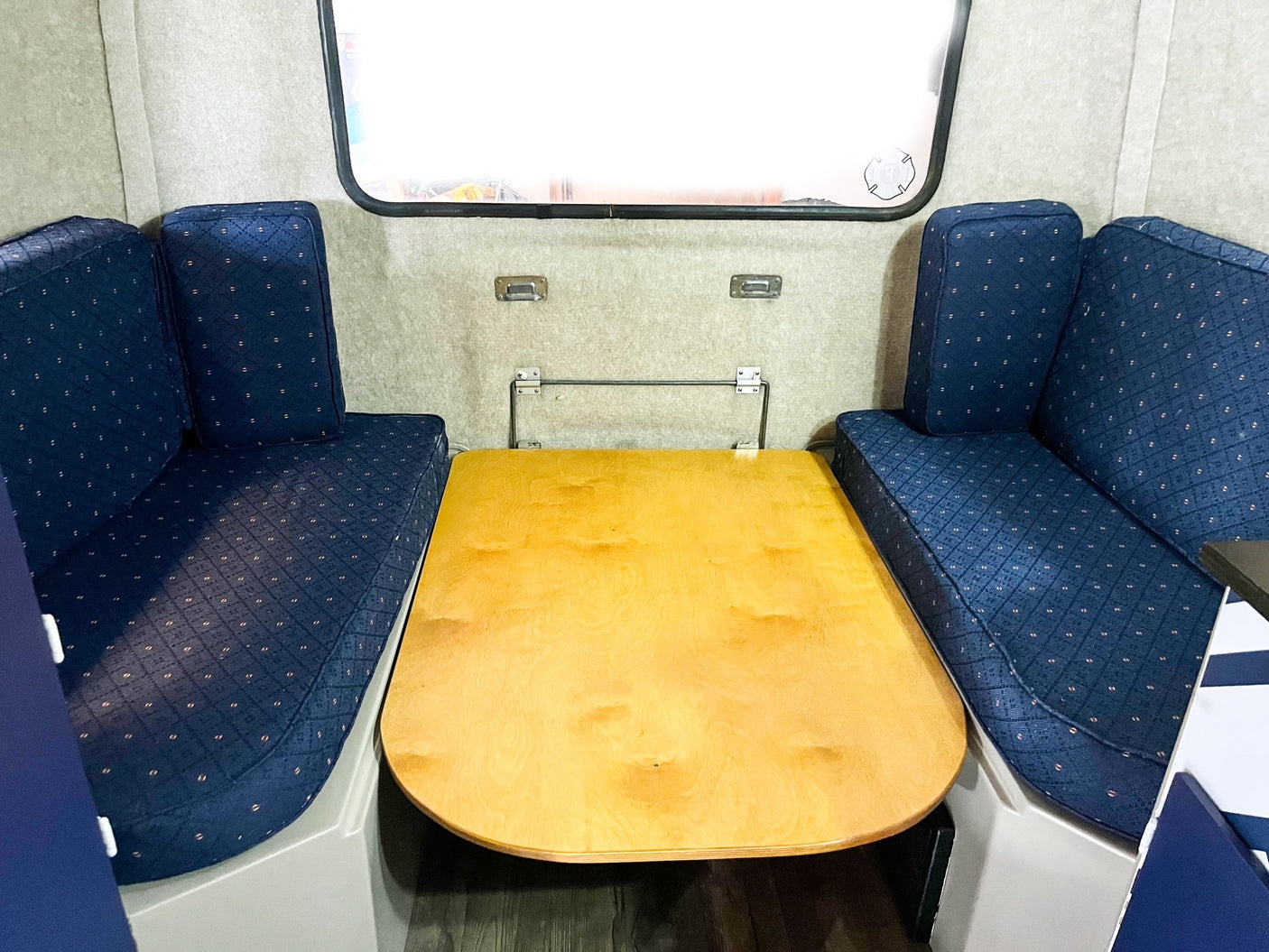 RV rental dinette with blue patterned benches and a light wood table. This convertible space serves dining & sleeping needs.