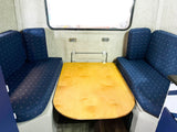 RV rental dinette with blue patterned benches and a light wood table. This convertible space serves dining & sleeping needs.