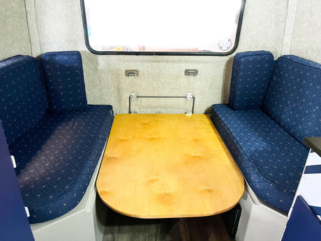 RV rental dinette with blue patterned benches and a light wood table. This convertible space serves dining & sleeping needs.