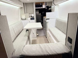 Modern camper van interior for your next RV rental, featuring a dinette, compact kitchen, and cozy gray seating.