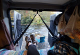 View from an RV rental: feet up, looking out the screened back doors at a rocky river and autumn trees. Camping scene.