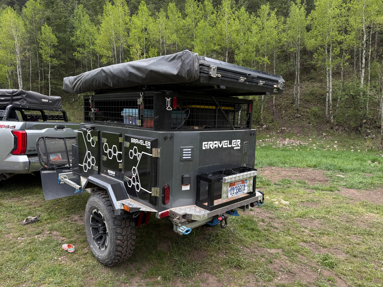 Adventure-ready overland trailer **RV rental** for camping, equipped with a rooftop tent, parked in a lush forest.