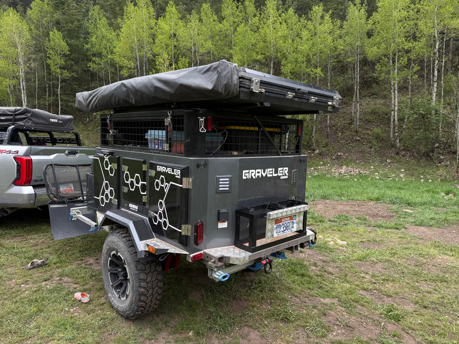 Adventure-ready overland trailer **RV rental** for camping, equipped with a rooftop tent, parked in a lush forest.