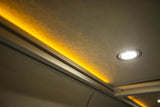 Cozy RV rental interior with warm accent strip lighting and bright spot light on a textured ceiling.