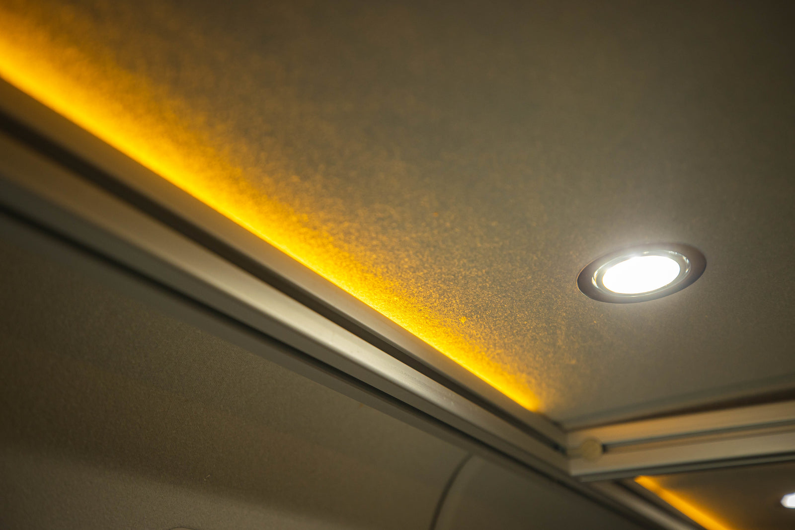 Cozy RV rental interior with warm accent strip lighting and bright spot light on a textured ceiling.
