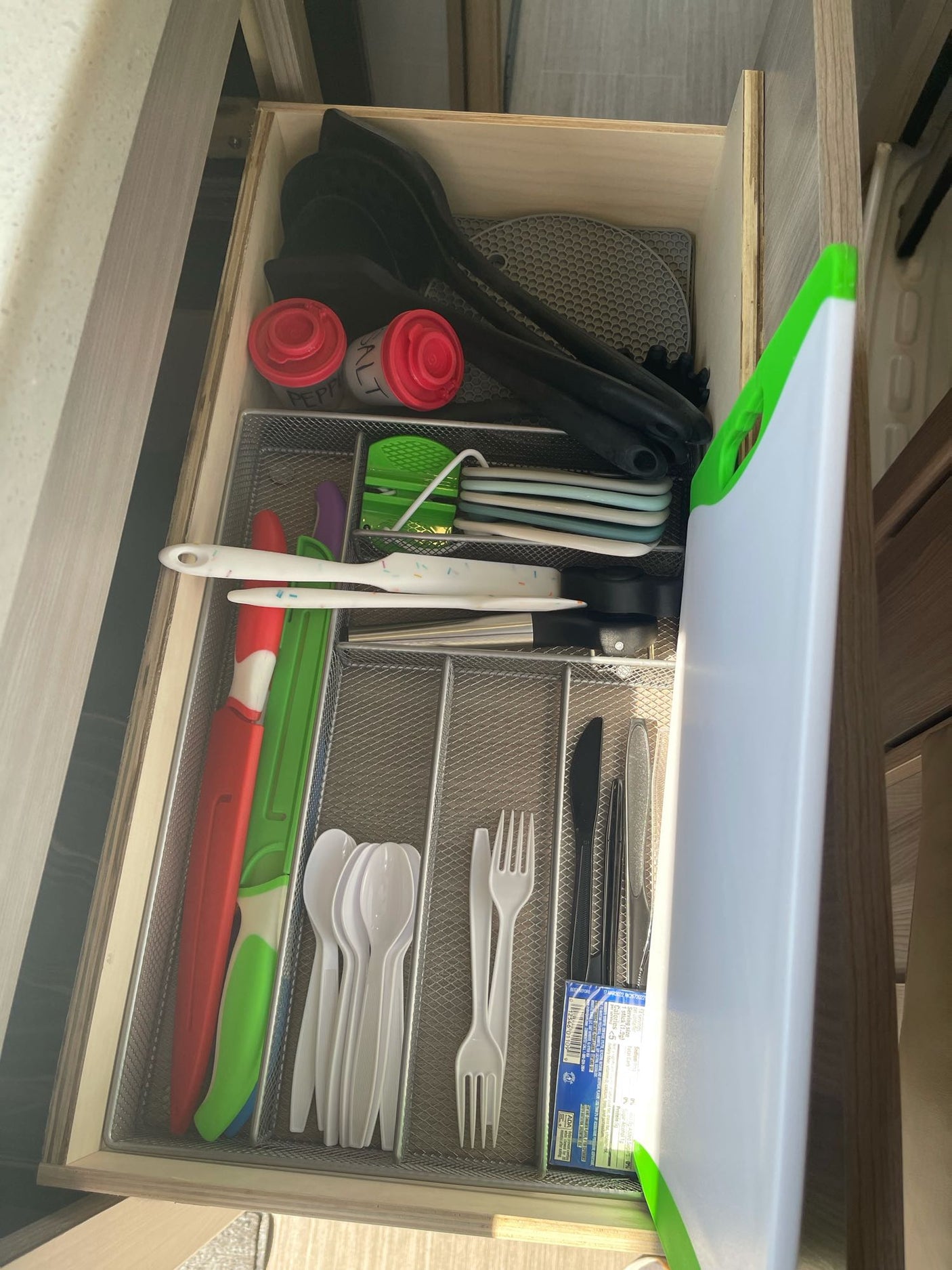 Organized kitchen drawer in an RV rental, featuring utensils, cutlery, salt/pepper shakers, and a cutting board for travel.