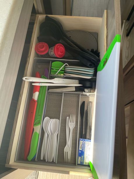 Organized kitchen drawer in an RV rental, featuring utensils, cutlery, salt/pepper shakers, and a cutting board for travel.