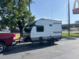 A red pickup tows a Coachmen Catalina RV rental in a parking lot, near a McDonald's. Ready for a road trip!