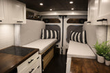 Spacious RV rental interior with facing light-grey bench seats, a modern kitchen with dark wood counter, and overhead lighting.
