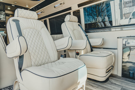 Luxurious RV rental interior featuring plush cream captain's chairs with diamond stitching, perfect for comfortable journeys.