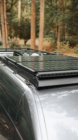 Nomadic RV rental van's roof with solar panels & a light bar, ready for off-grid adventures in the woods.