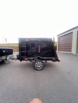 This custom black camper trailer, hitched to a truck, is perfect for an rv rental adventure, parked near storage units.
