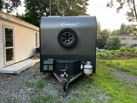 This sleek gray teardrop trailer, a perfect RV rental option, is set up for camping with its spare tire, propane, and power hookup.