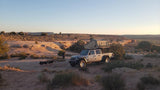 RV rental adventure! A Jeep Gladiator with rooftop tent is set up for camping in a vast, sunny desert landscape.
