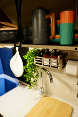 An RV rental's efficient kitchen setup: shelf with cookware & cups, sink with soap caddy & paper towels.