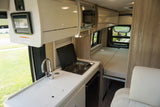 Bright, modern rv rental interior with kitchen, including sink, stove, microwave, fridge, and a bed/seating area.