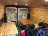 Spacious, wood-paneled RV rental interior features a folding table, bed platform, custom map doors, and seating, ideal for family travel.