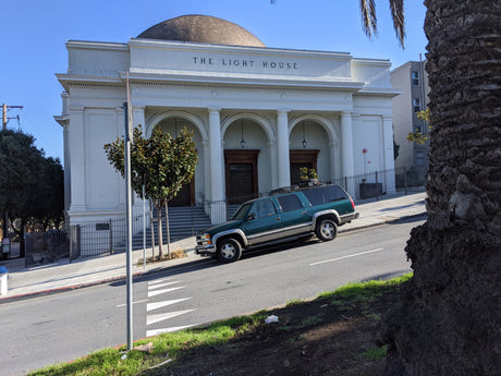 Green SUV parked near 'The Light House' building on a steep street. Consider an rv rental for your next journey.