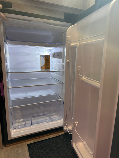 An RV rental's mini-fridge, open and clean, with clear shelves & a baking soda box. Ready for your groceries!