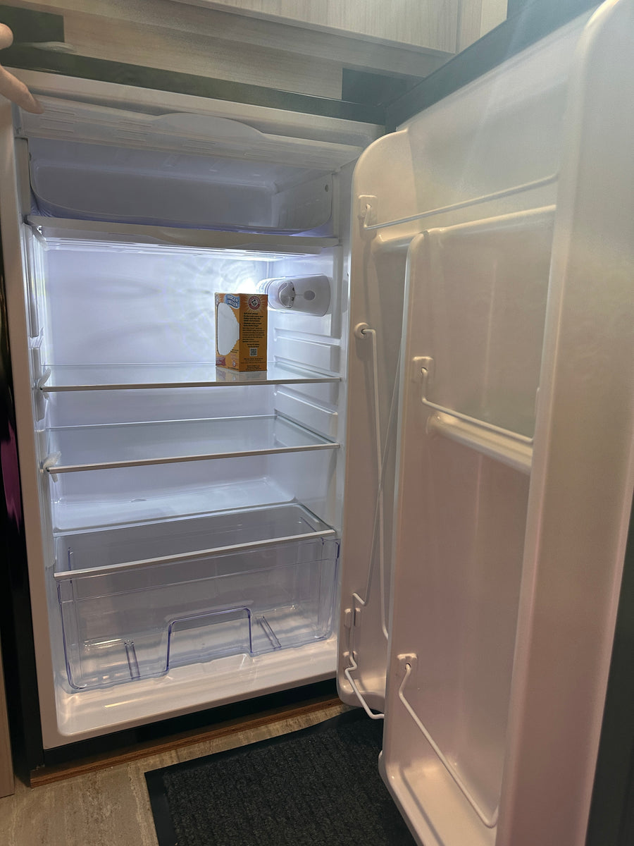 An RV rental's mini-fridge, open and clean, with clear shelves & a baking soda box. Ready for your groceries!