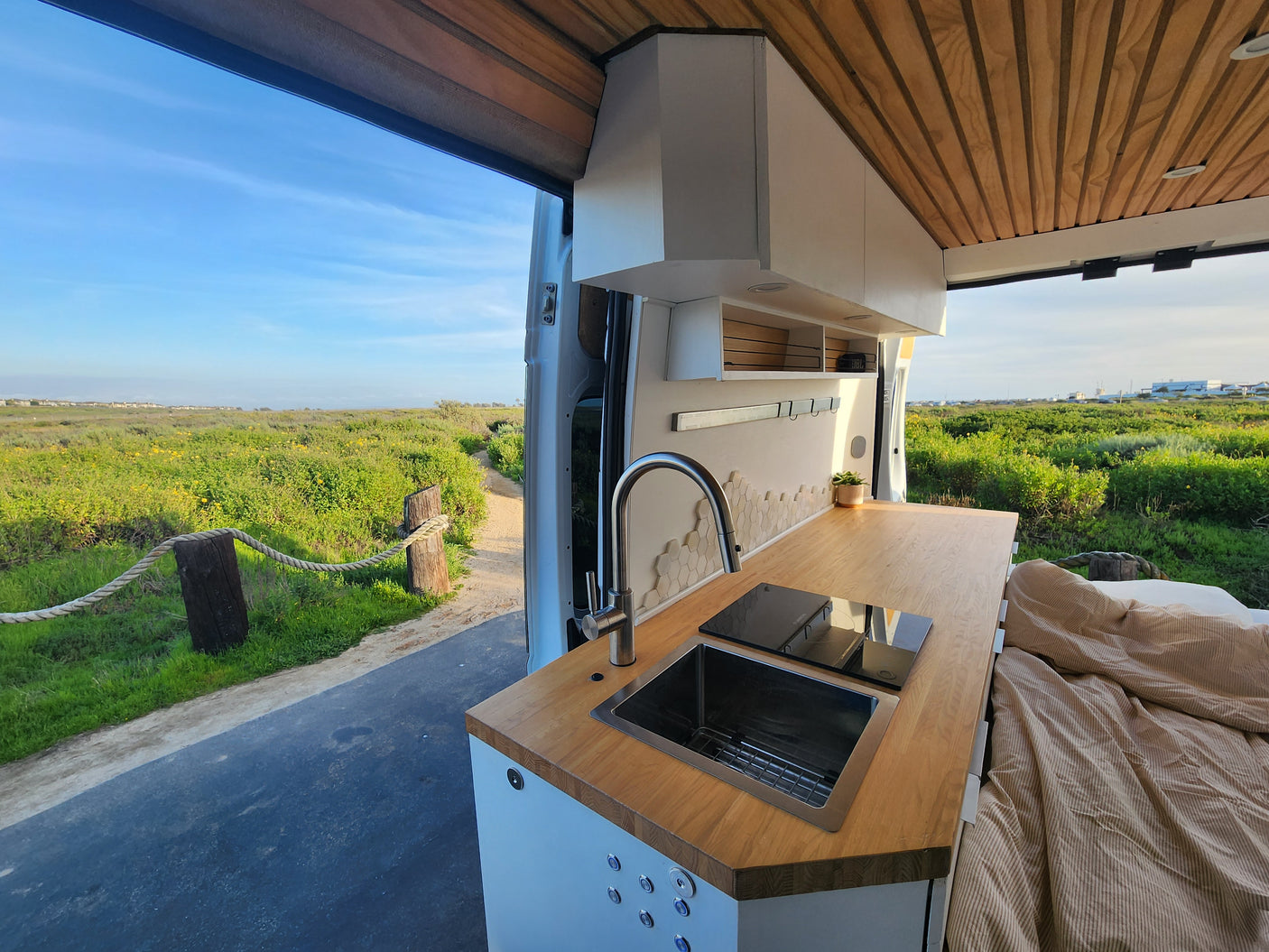 Enjoy adventure in this rv rental. Camper van interior with a modern kitchen, cozy bed, and vast grassy field view.