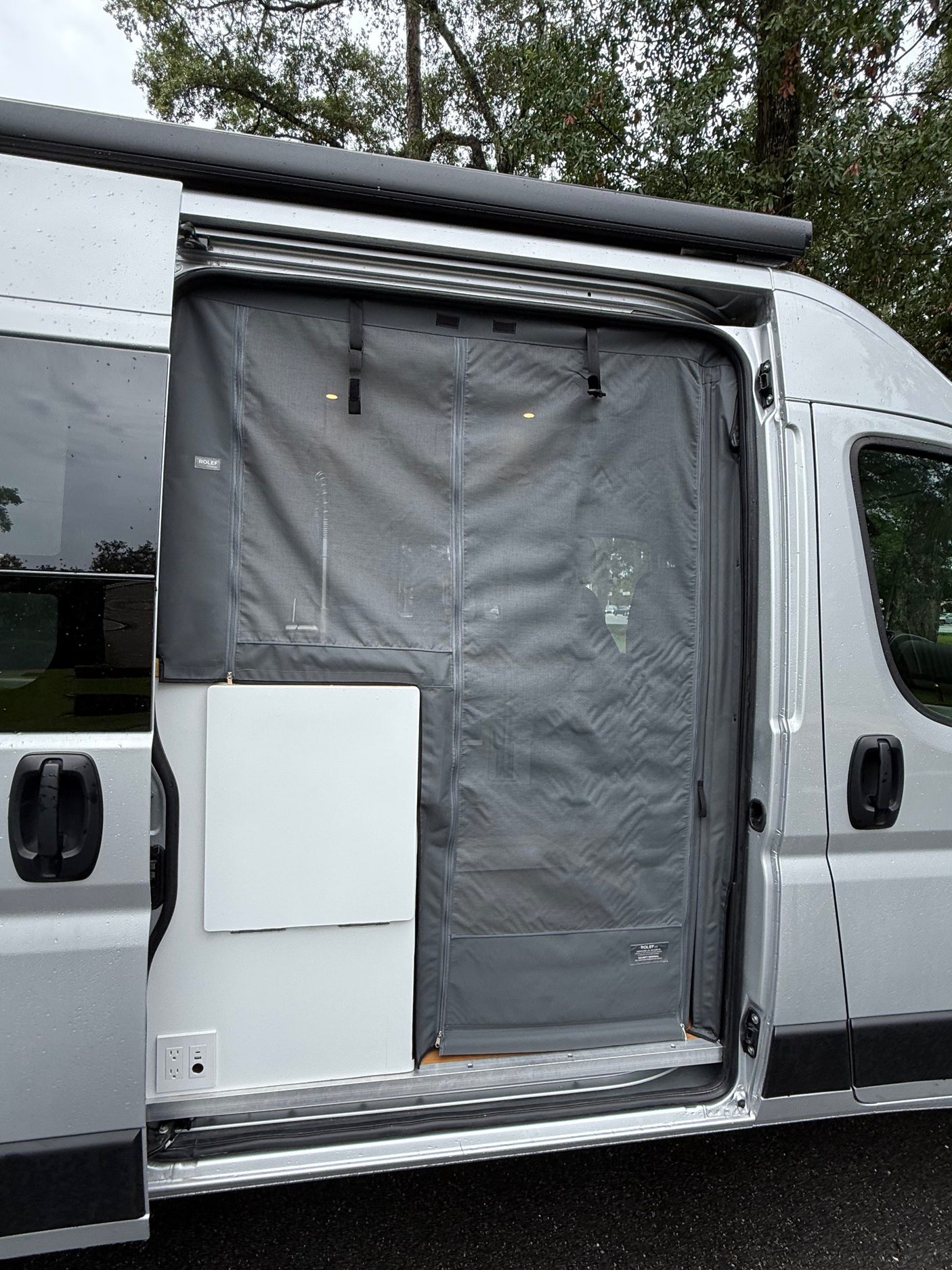 RV rental with sliding door open, revealing a gray Rolef mesh screen, interior power outlets, and an awning.