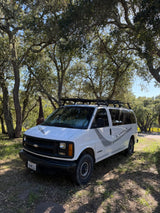 White Chevy camper van, great for an rv rental, parked under mossy oak trees with a giraffe statue in background.